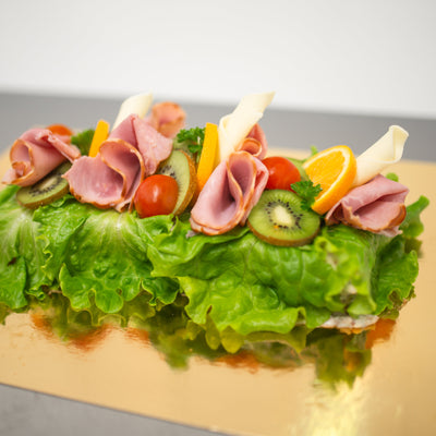 En aptitretande smörgåstårta med generöst beströdd med skinka, kiwi och salladsblad på toppen
